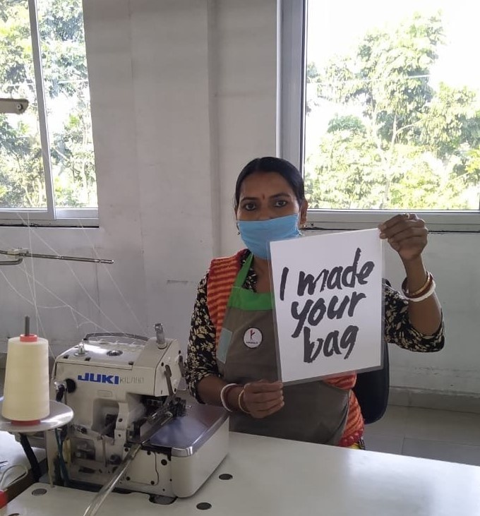 A female garment worker, at work wearing a blue surgical mask and holding a black and white poster which says 