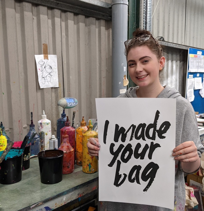 A woman holding a I Made Your Bag poster 